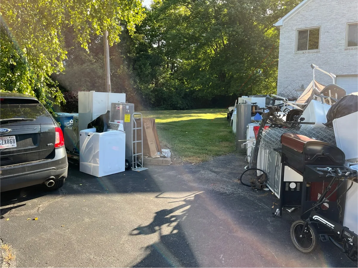 Two old refrigerators, water heaters, and scrap metal staged on an Indianapolis driveway before pickup
