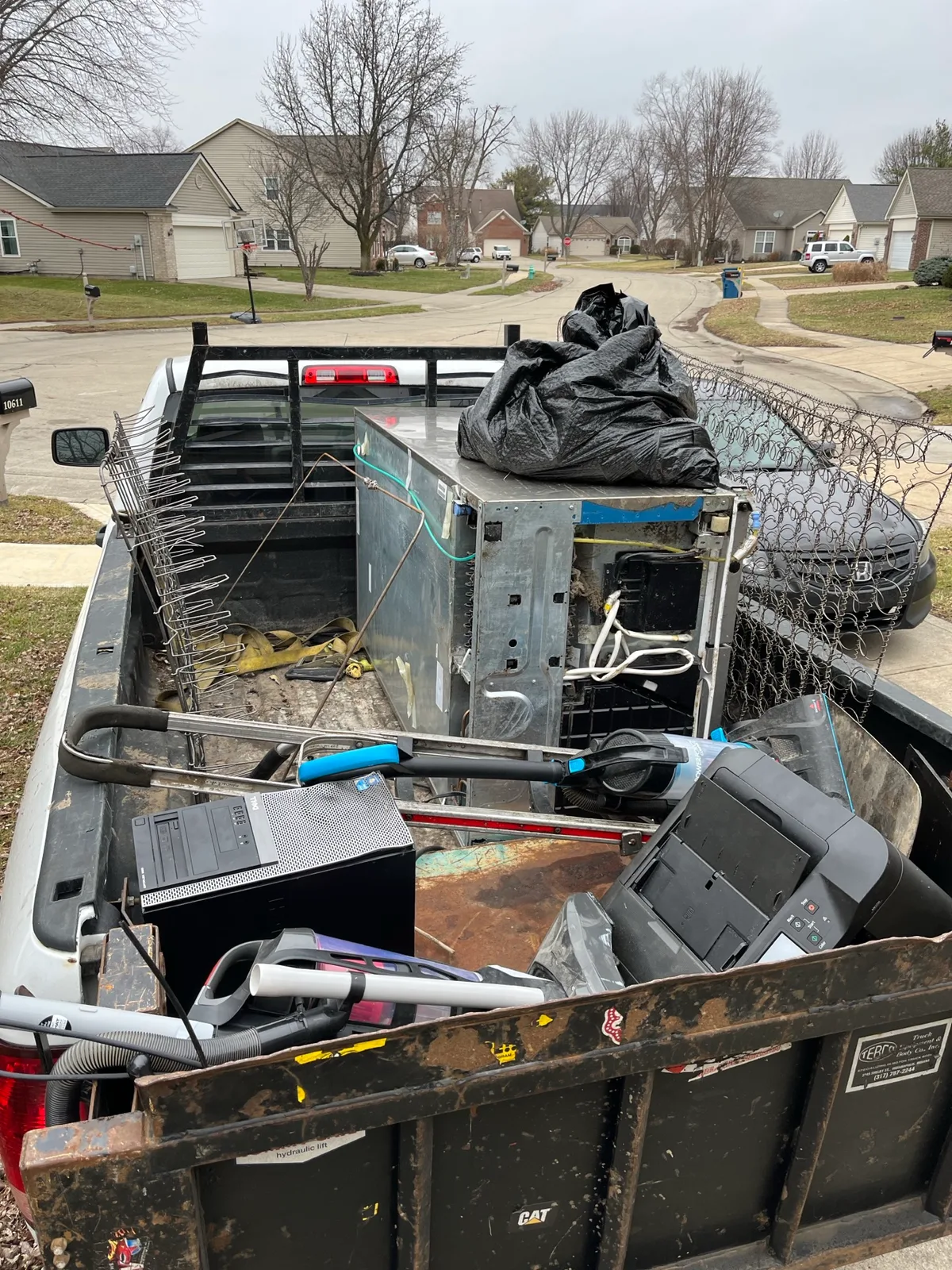A loaded Indy Pickup 1111 dump bed with a desktop computer, printer, vacuum, and scrap metal cleared from an Indianapolis garage